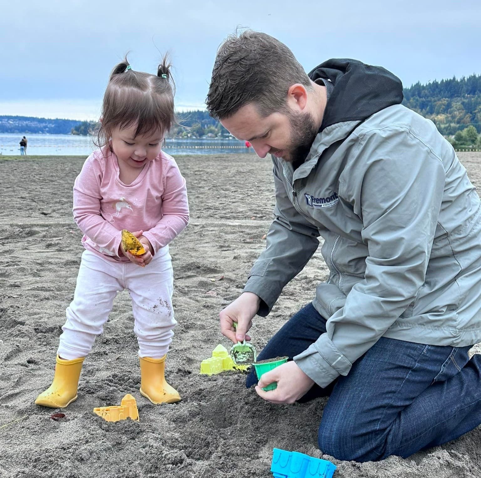 Jeff and his daughter Natalia building sand castles at the lake, with Washington's hills in the background